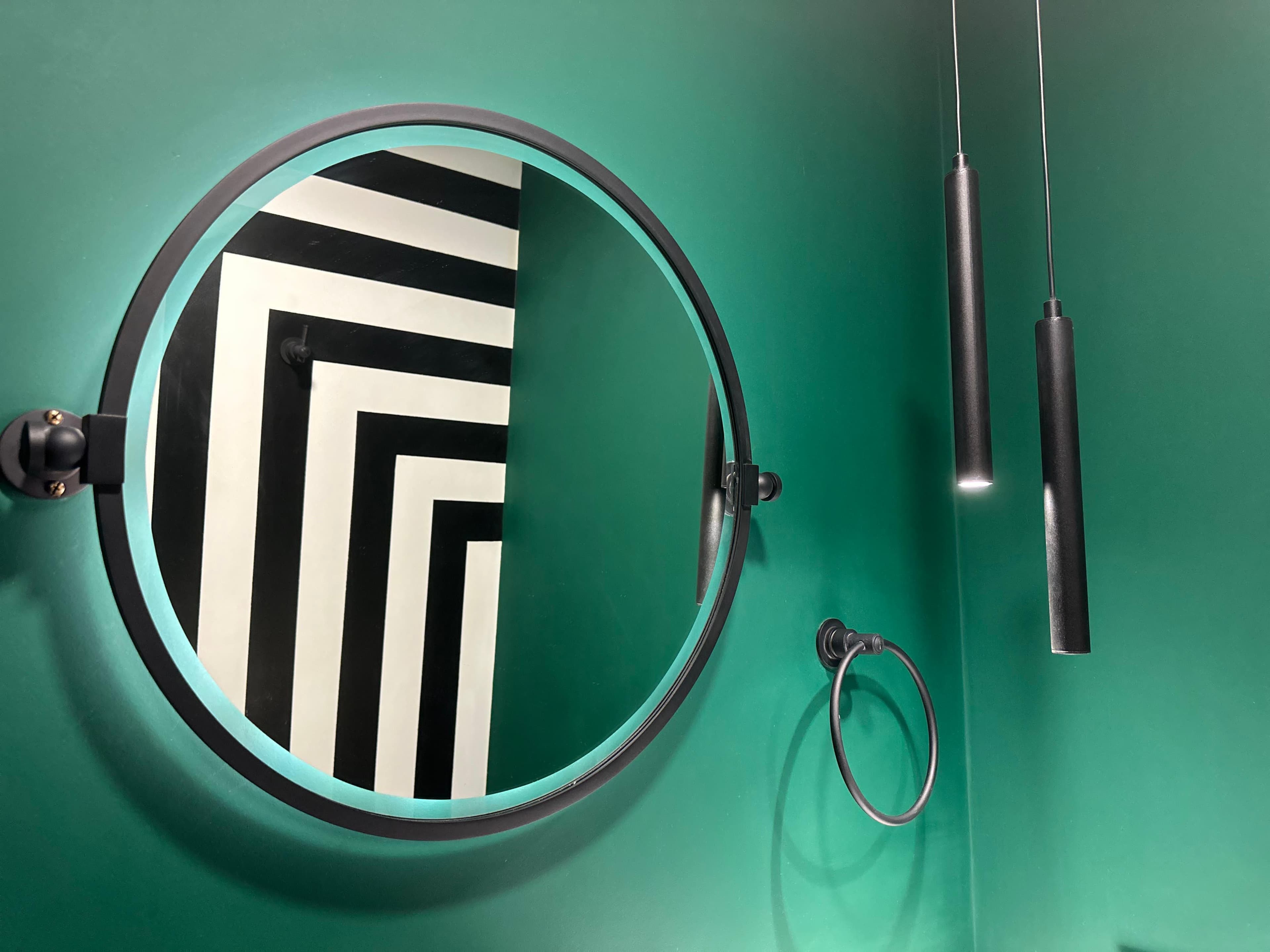 Baño del proyecto Charlone: espejo redondo con marco negro sobre pared verde profundo, reflejando un revestimiento a rayas