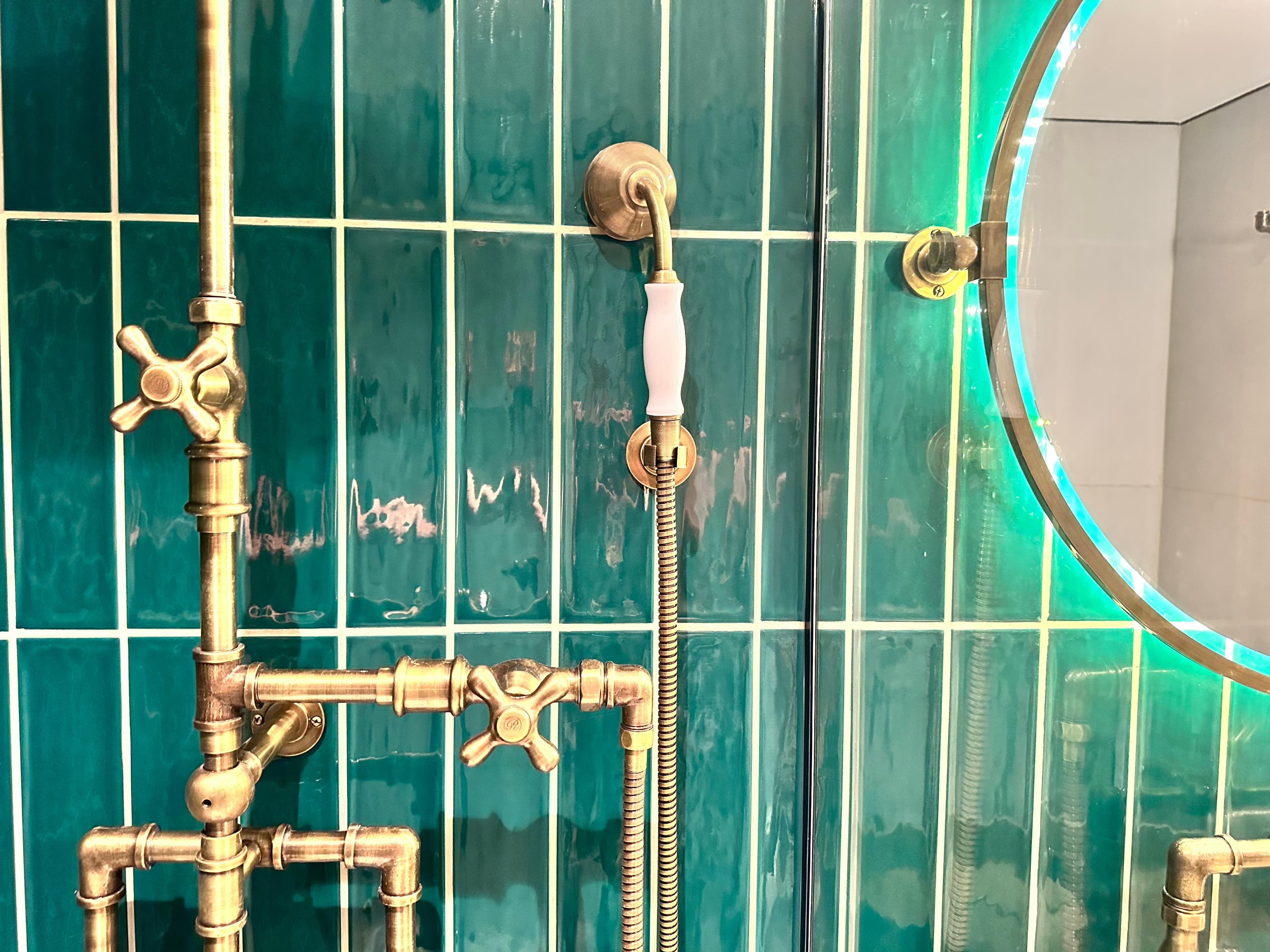 Baño del proyecto Charlone con grifería dorada sobre revestimiento verde azulado